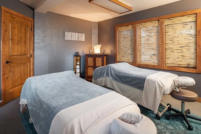 Couples massage room at Blue Sky Massage in Winter Park with twin massage tables, a rustic wood door, and bamboo window blinds