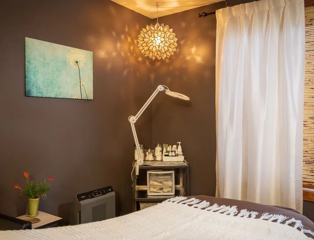 Quiet single treatment room at Blue Sky Massage in Winter Park — brown accent wall, dandelion canvas, capiz pendant lamp, and an adjustable magnifier
